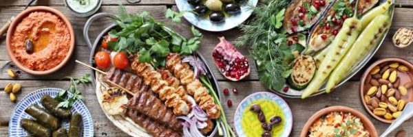 Middle eastern, arabic or mediterranean dinner table with grilled lamb kebab, chicken skewers  with roasted vegetables and appetizers variety serving on rustic outdoor table. Overhead view.